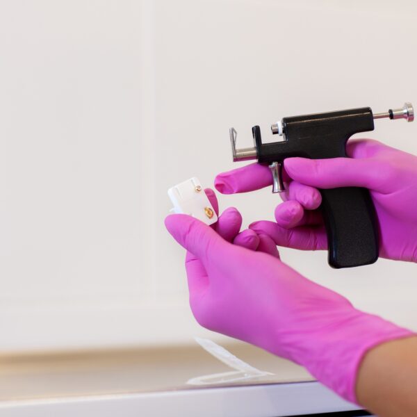 Female cosmetologist holding earrings and ear piercing gun