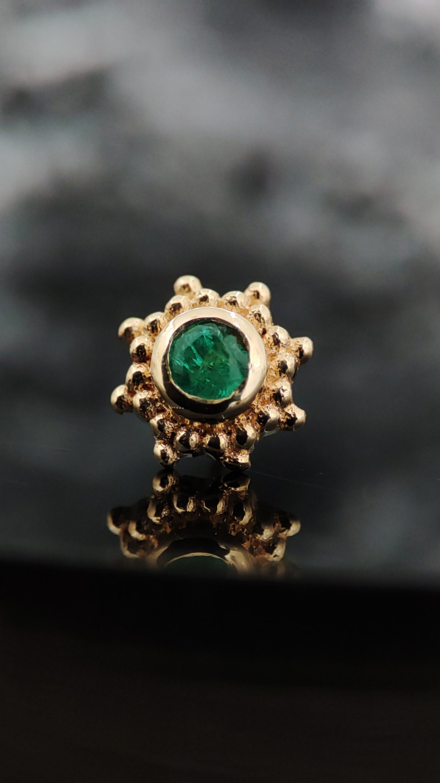 NAGA Peshavia Green Emerald – pirsing nakit od 18K zlata NAGA Peshavia Green Emerald – zlatni ukrasni deo za pirsing sa zelenim kamenom i dekorativnim detaljima
